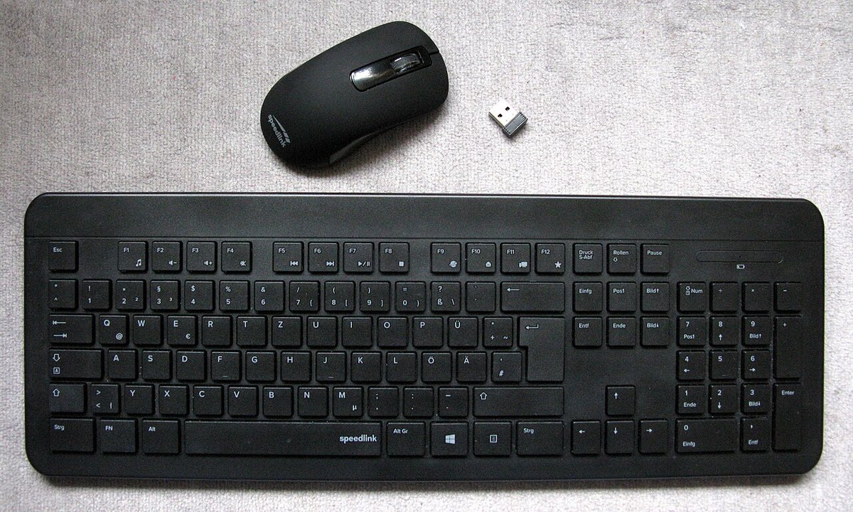 Bàn phím không dây màu đen cùng chuột và cục thu USB đặt trên bàn